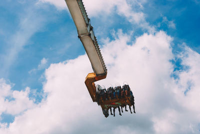 Low angle view of people enjoying suspended ride at amusement park against cloudy sky