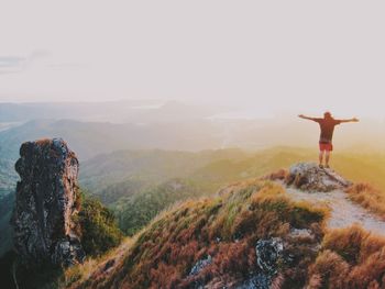 Rear view of man standing on mountain with arms outstretched