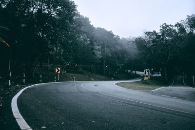 Road by trees in city against sky