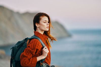 Young woman looking away while standing by sea against sky