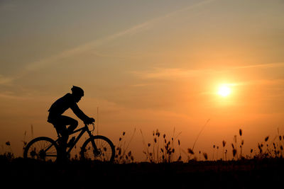 Silhouette man riding bicycle against sky during sunset