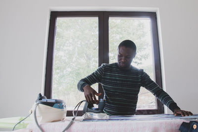 Portrait of young man standing by window at home