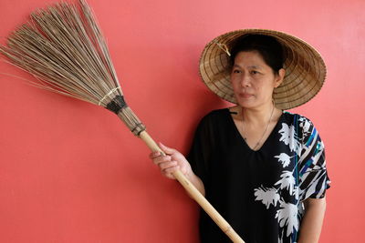 Portrait of woman holding hat against red background