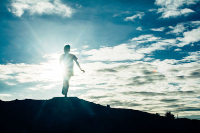 Low angle view of silhouette man standing on rock against sky
