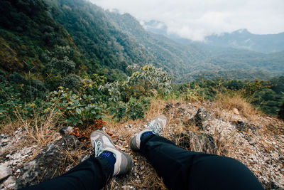 Low section of person wearing shoes sitting on cliff