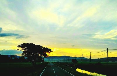 Road by trees against sky during sunset