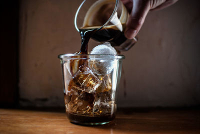 Cropped image of person pouring coffee on drinking glass