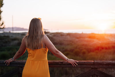 Rear view of woman standing against sky during sunset