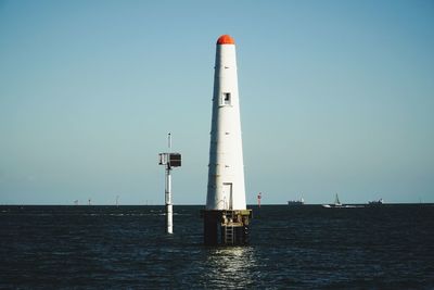 Lighthouse by sea against clear sky