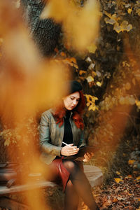 Young woman using digital tablet while sitting near tree