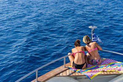 Rear view of women in bikini sitting by railing in boat on sea