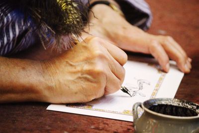 Cropped image of woman writing on paper with fountain pen on table