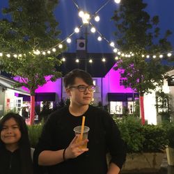 Portrait of young man standing against illuminated plants at night