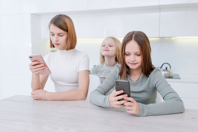 Portrait of happy friends using mobile phone while sitting on bed at home