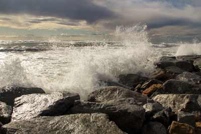 Scenic view of sea and waves splashing against the rocks in windy day