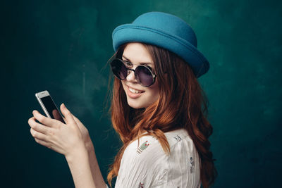 Portrait of young woman using mobile phone against wall
