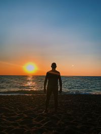 Rear view of silhouette man standing on beach during sunset