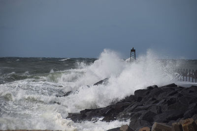 Waves splashing on rocks against clear sky