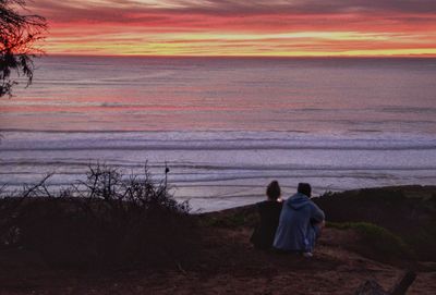 Rear view of silhouette friends on beach against sky during sunset