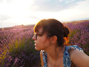 Portrait of woman with pink flowers on field against sky