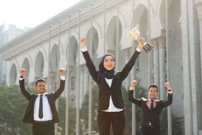 Portrait of young woman with arms raised standing in city