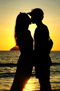 Silhouette people at sea against sky during sunset