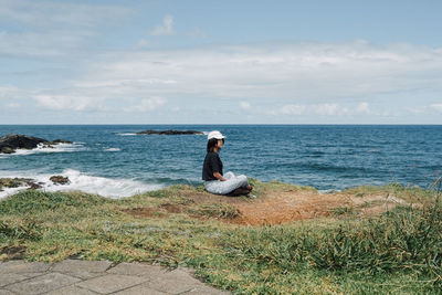 Rear view of woman sitting on rock by sea against sky