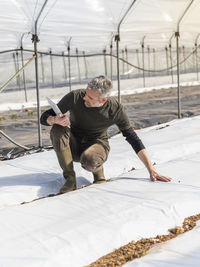 Male farmer using digital tablet while planting in greenhouse