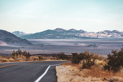 Road leading towards landscape and mountains against sky