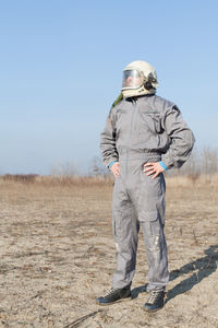 Man in uniform and helmet standing on field against sky