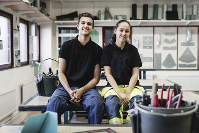 Portrait of confident high school students sitting on table in workshop