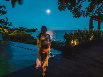 Full length of woman standing against sea during dusk