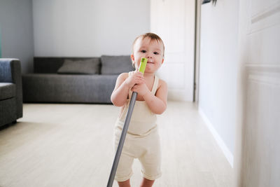 Toddler with broom sweeps floor in bright room in scandinavian style, montessori development