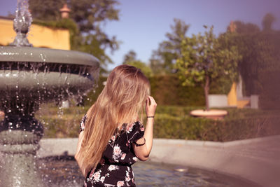 Side view of young woman standing by fountain