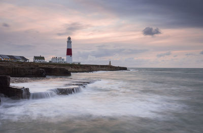Lighthouse by sea against sky during sunset