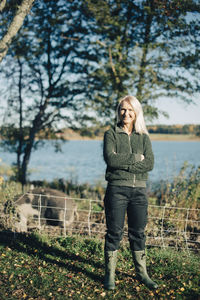 Full length portrait of female farmer standing arms crossed on organic farm with pig in background