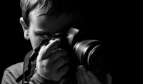 Close-up of boy photographing with camera against black background