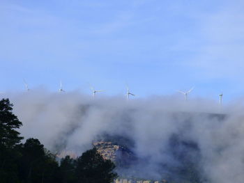 Windmills on mountain during foggy weather against blue sky