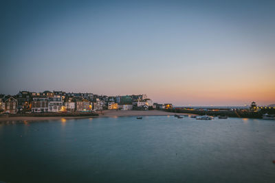 Illuminated cityscape by sea against sky