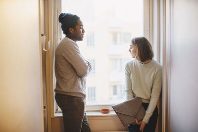 Young friends talking by window in college dorm corridor