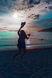 Man jumping at beach against sky during sunset