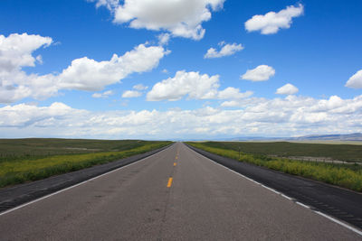 Empty road amidst field against cloudy sky