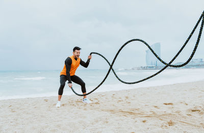 Male athlete exercising with rope at beach