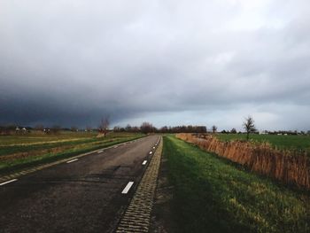 Empty road amidst field against sky