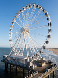 Ferris wheel by sea against clear blue sky