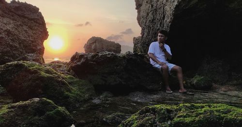 Man standing on rock against sky during sunset