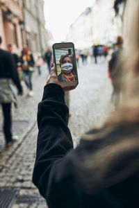 Young woman having video call talking while walking downtown in the evening wearing the face mask