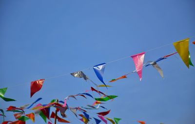 Low angle view of flags against clear blue sky