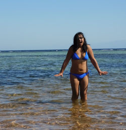 Full length of young woman standing on beach against clear sky