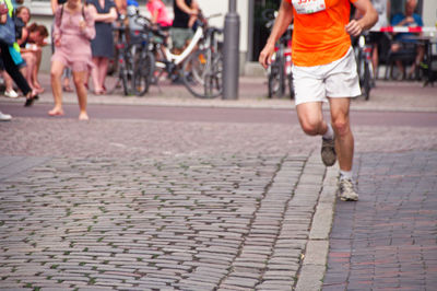 Low section of athlete running marathon on street with people cheering in background